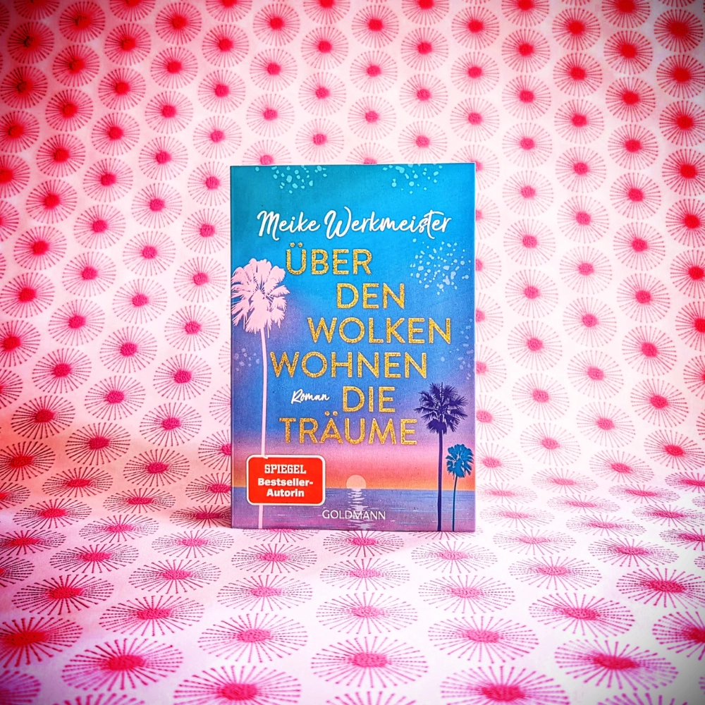 Das Foto zeigt die Taschenbuch-Ausgabe des Romans „Über den Wolken wohnen die Träume“ von Meike Werkmeister, der im Goldmann-Verlag veröffentlicht wurde. Das Buch steht vor einem gemusterten Papier-Hintergrund.