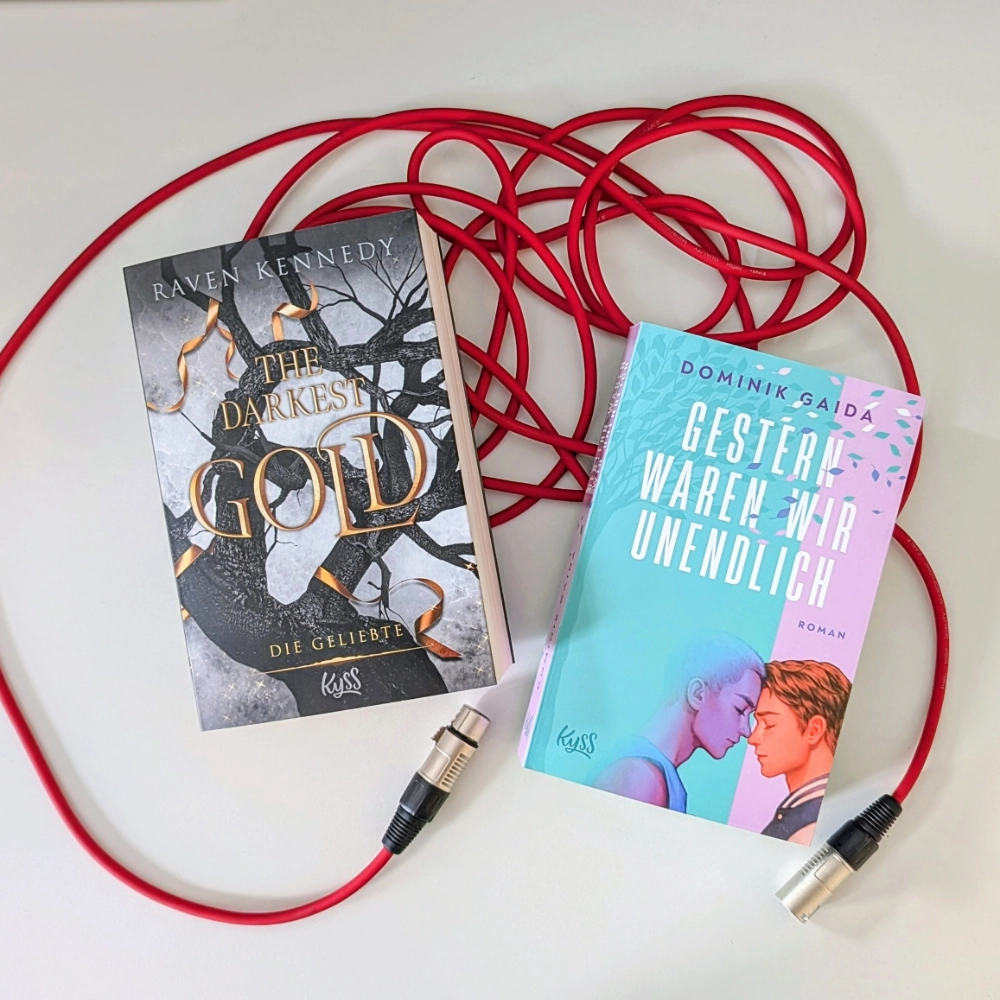 Das Bild zeigt links den Roman THE DARKEST GOLD: DIE GELIEBTE von Raven Kennedy  und rechts daneben den Roman GESTERN WAREN WIR UNENDLICH von Dominik Gaida, beide erscheinen bei KYSS. Die Bücher liegen auf einem roten Mikrofonkabel.