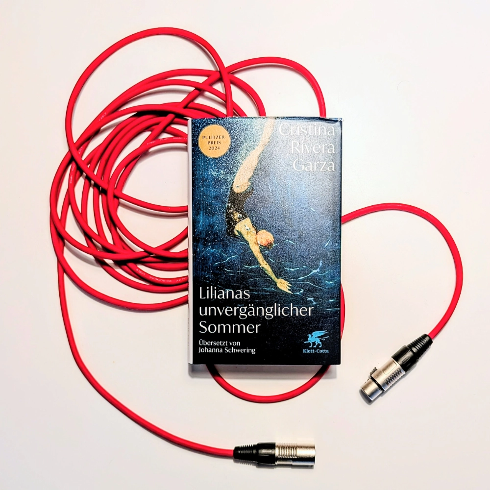 Das Foto zeigt den Roman LILIANAS UNVERGÄNGLICHER SOMMER von Cristina Rivera Garza, in der Übersetzung von Johanna Schwering erschienen bei Klett-Cotta. Das Buch liegt auf einem roten Mikrofonkabel.