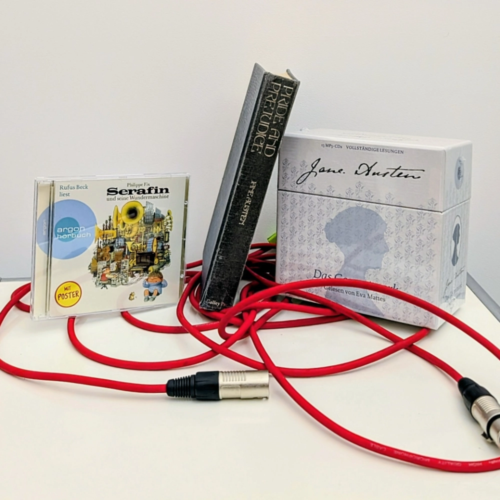 Das Bild zeigt links die CD-Version des Hörbuchs SERFAIN UND SEINE WUNDERMASCHINE von Philippe Fix, in der Mitte eine Buchausgabe von Jane Austens Roman PRIDE AND PREJUDICE und rechts daneben eine CD-Box mit den gesammelten Werken von Jane Austen; die Hörbücher sind alle bei Argon erschienen und stehen auf einem roten Mikrofonkabel.