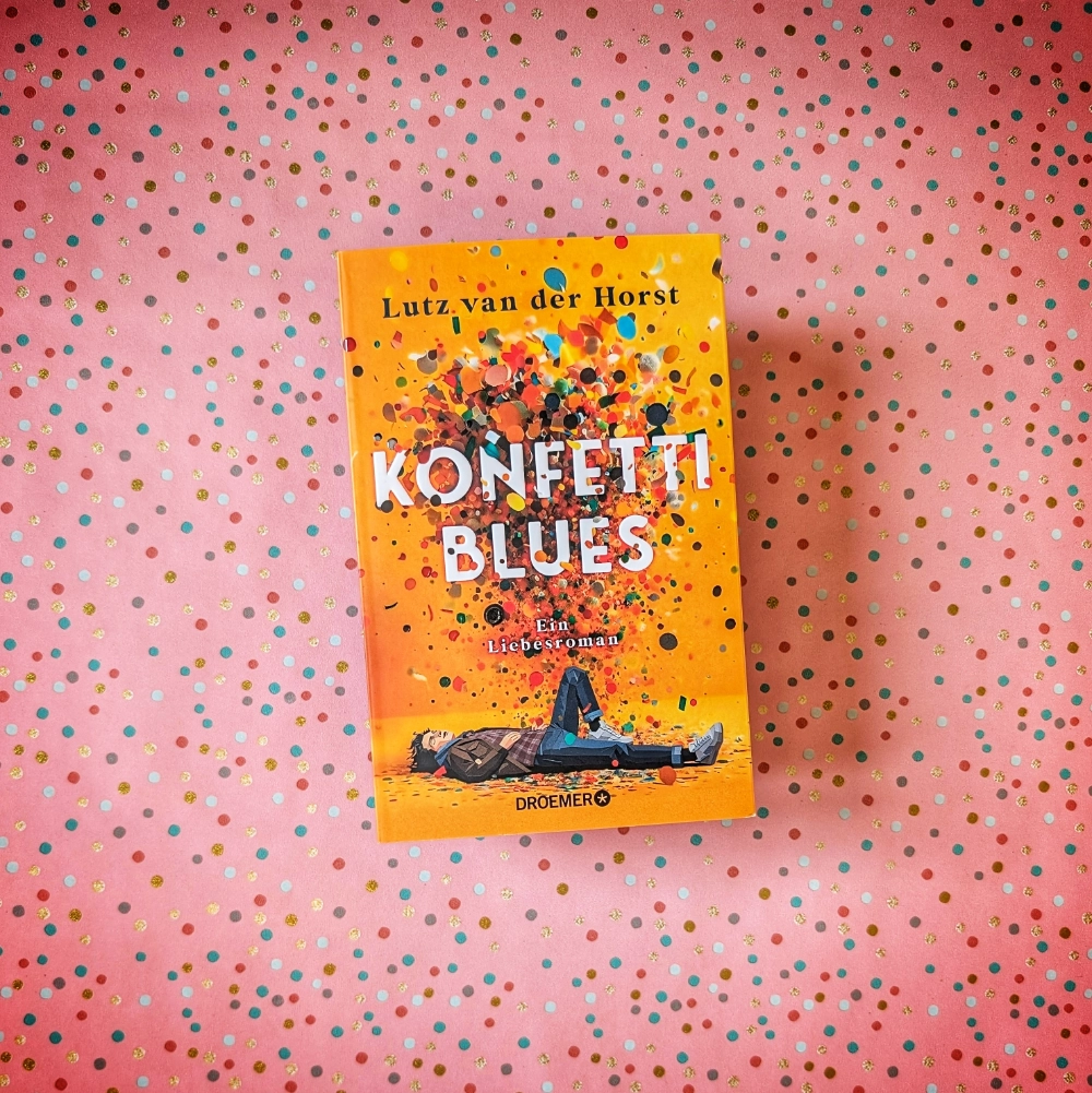 Das Foto zeigt den Roman KONFETTIBLUES von Lutz van der Horst; das Buch liegt auf einem gemusterten Papierhintergrund