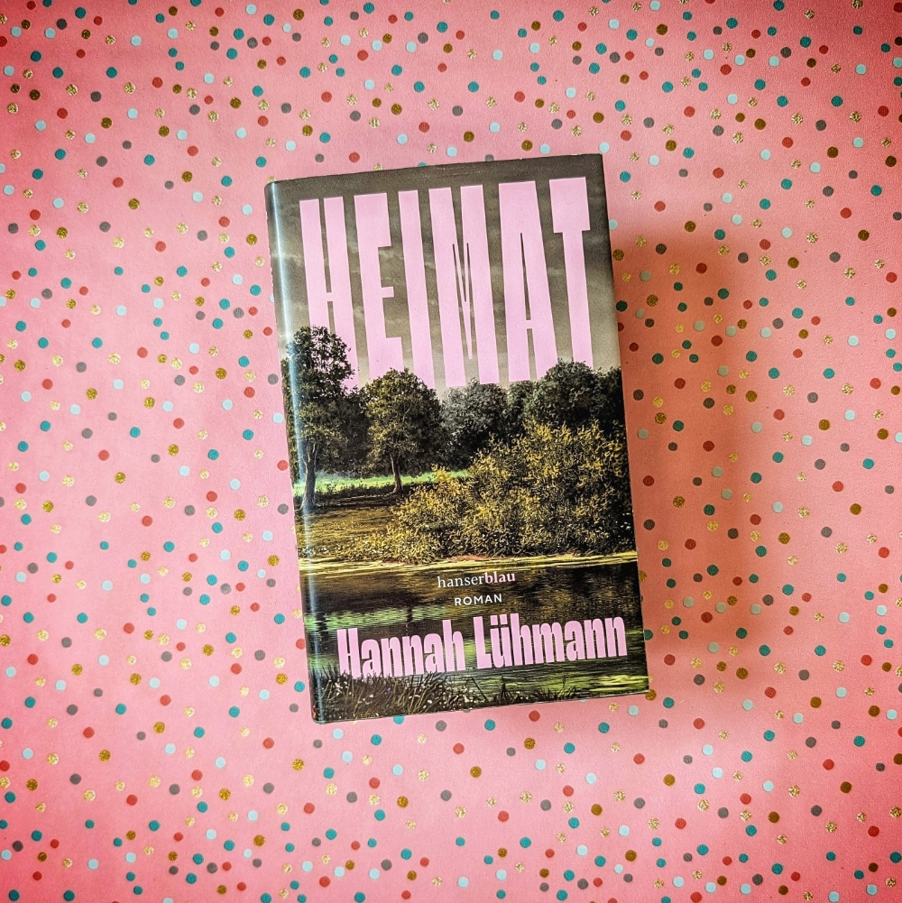 Das Foto zeigt das Buch HEIMAT von Hannah Lühmann; es liegt auf einem gemusterten Papierhintergrund.