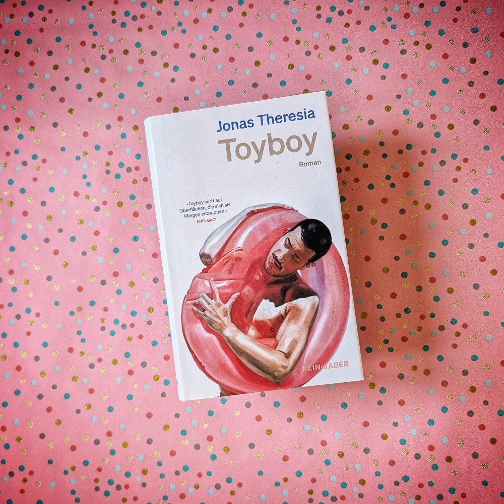 Das Foto zeigt das Buch TOYBOY von Jonas Theresia, das auf einem gemusterten Papierhintergrund liegt.
