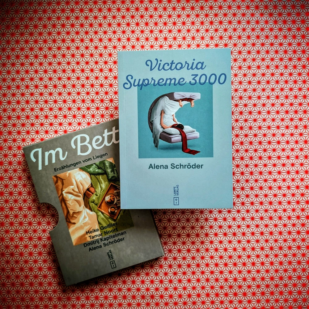Das Foto zeigt das Minibuch „Victoria Supreme 3000“ von Alena Schröder. Es ist Teil des Buchschubers „Im Bett – Erzählungen vom Liegen“, erschienen im Lampe Verlag. Das Minibuch und der Buchschuber liegen auf einem gemusterten Papierhintergrund.