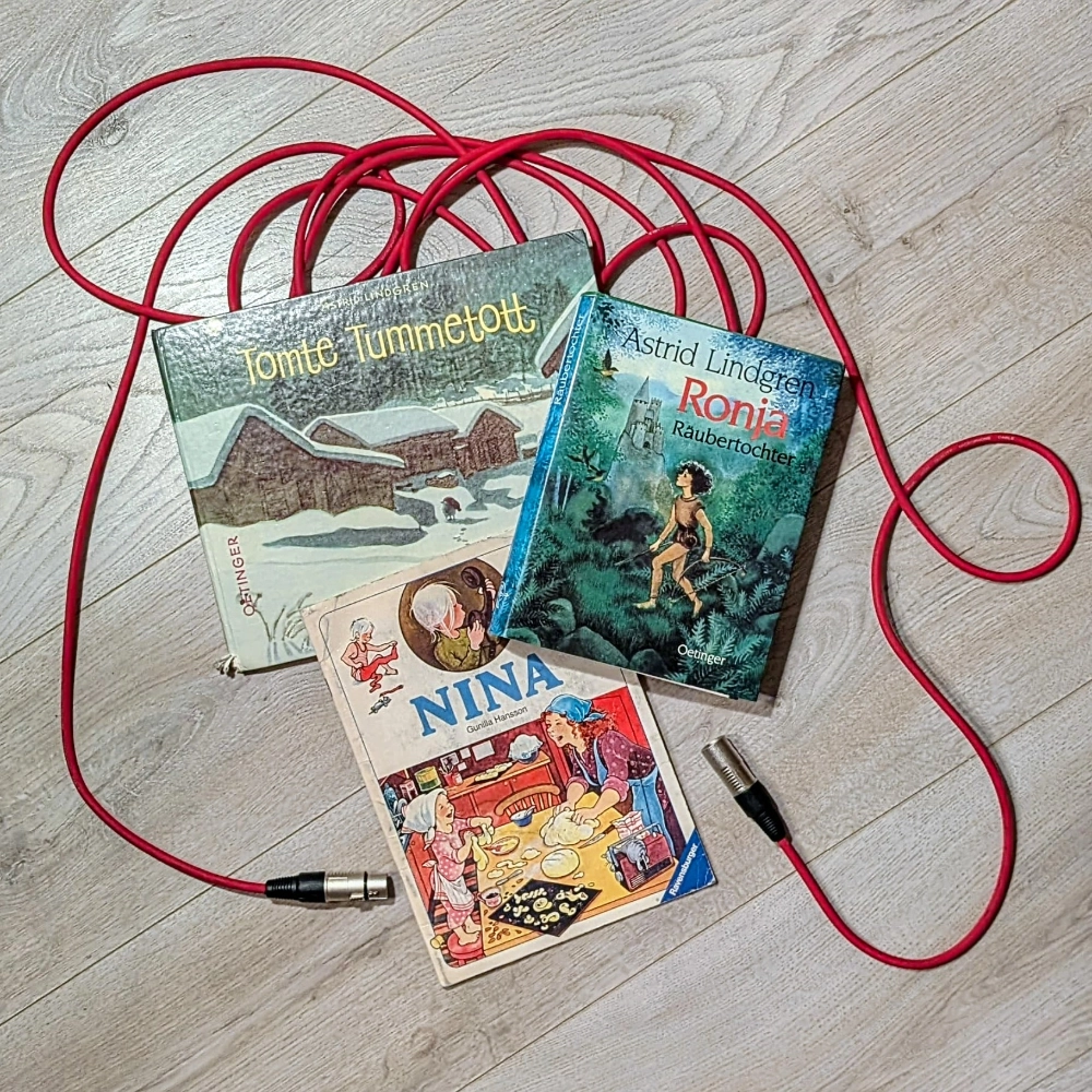 Das Foto zeigt drei Kinderbücher, die auf einem roten Mikrofonkabel liegen: RONJA RÄUBERTOCHTER und TOMTE TUMMETOTT von Astrid Lindgren sowie NINA von Gunilla Hansson.
