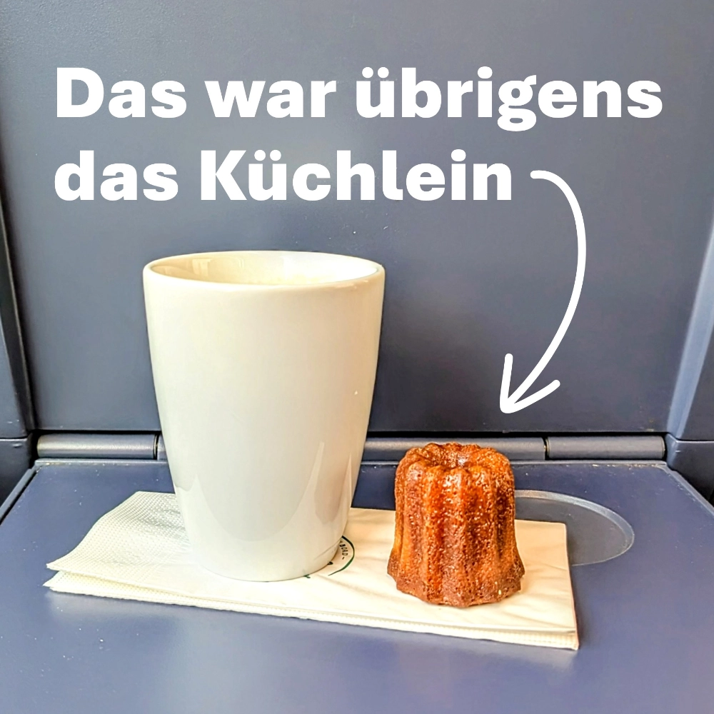 Das Foto zeigt einen Kaffeebecher der Deutschen Bahn auf einem Ausklapp-Tisch in einem ICE; rechts daneben steht das kleine Küchlein, das im Text erwähnt wird.