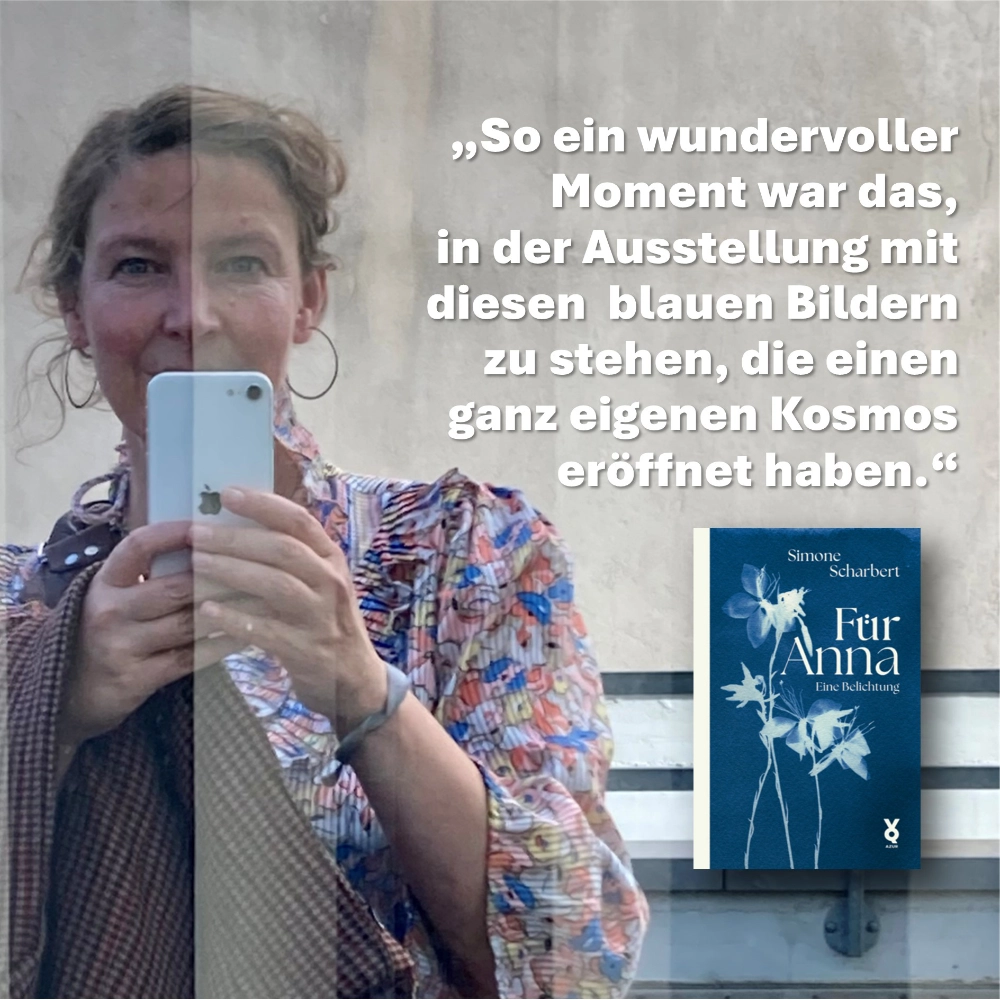 Das Bild zeigt ein Selfie der Autorin Simone Scharbert, die sich in einer spiegelnden Scheibe selbst fotografiert hat; unter ihrem Zitat „So ein wundervoller Moment war das, in der Ausstellung mit diesen blauen Bildern zu stehen, die einen ganz einen Kosmos eröffnet haben“ ist der Umschlag ihres Buchs „Für Anna – Eine Belichtung“ zu sehen.