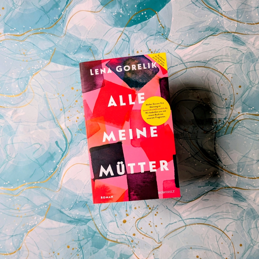 Das Foto zeigt die Hardcover-Ausgabe des Buchs „Alle meine Mütter“ von Lena Gorelik, das bei Rowohlt veröffentlicht wurde. Das Buch liegt auf einem gemusterten Papier-Hintergrund.