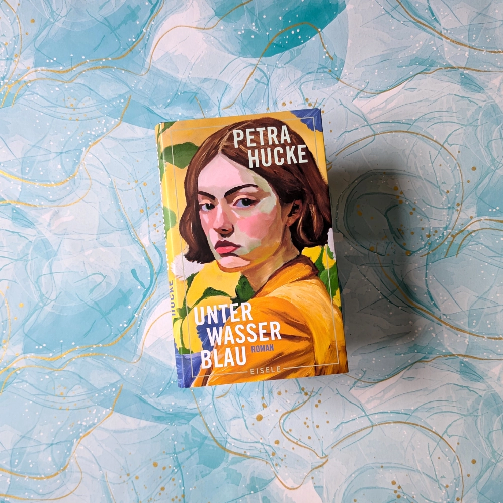 Das Foto zeigt die Hardcover-Ausgabe des Romans „Unterwasserblau“ von Petra Hucke, der im Eisele Verlag veröffentlicht wurde. Das Buch liegt auf einem gemusterten Papier-Hintergrund.