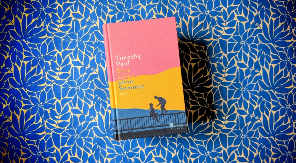 Das Foto zeigt das Buch EINE LIEBE OHNE SOMMER von Timothy Paul, das auf einem gemusterten Papierhintergrund liegt.