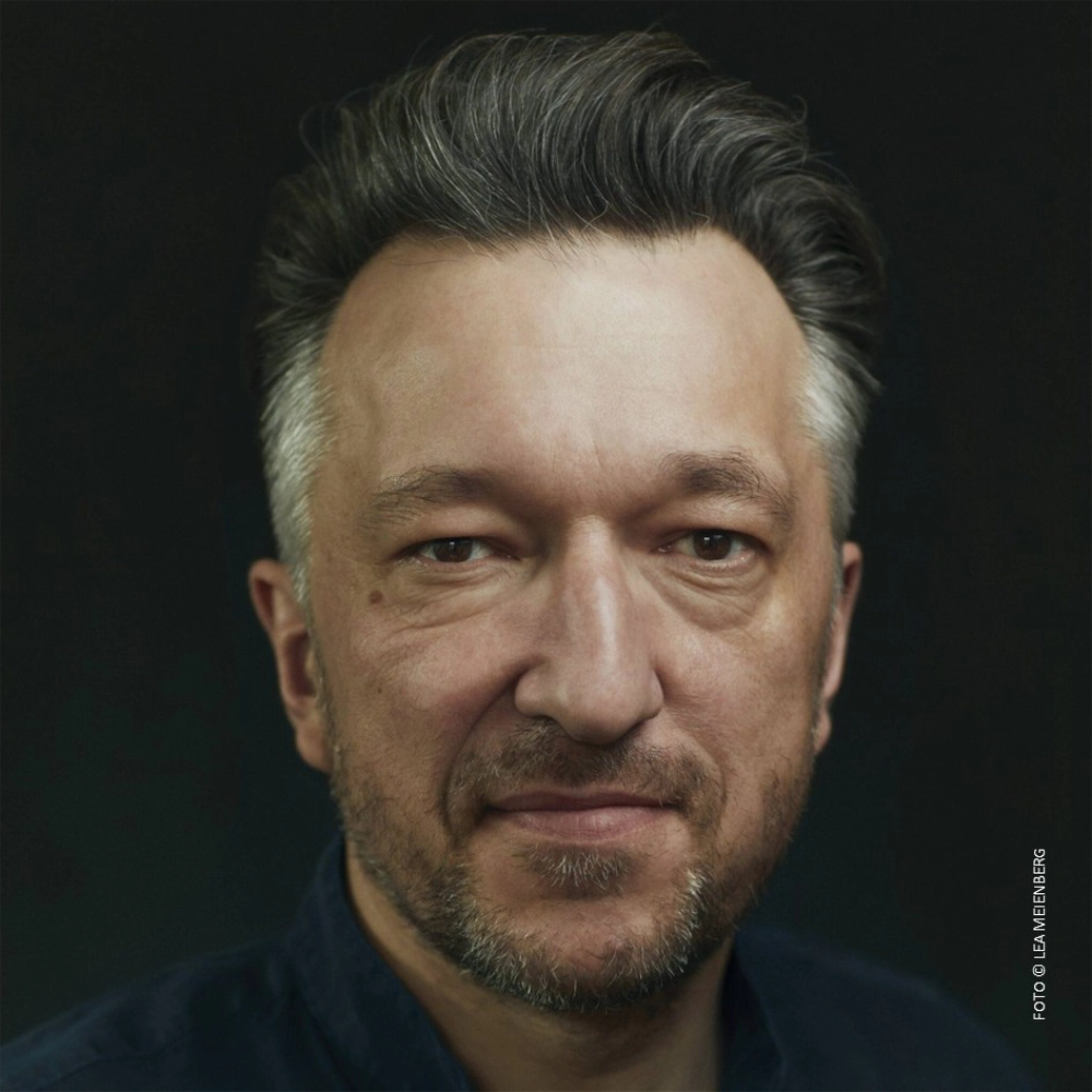 Das Foto zeigt den Autor Lukas Bärfuss vor einem schwarzen Hintergrund.